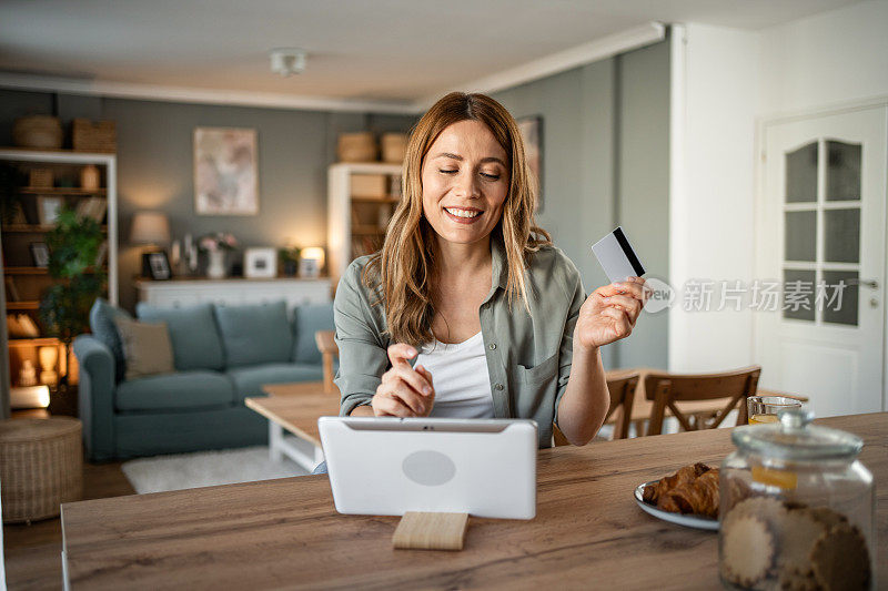 一位女士坐在房间里，用数码平板电脑和信用卡，通过网上银行查看每月的预算