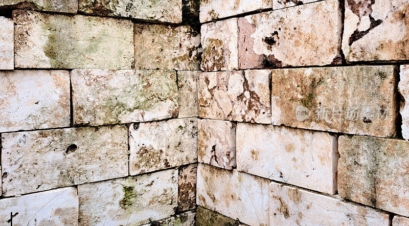 风化的米色石灰石砌块墙壁背景与洞，污垢和苔藓生长。这些石头是一座废弃建筑遗留下来的，彼此堆叠在一起，给人一种质朴的古老感觉。