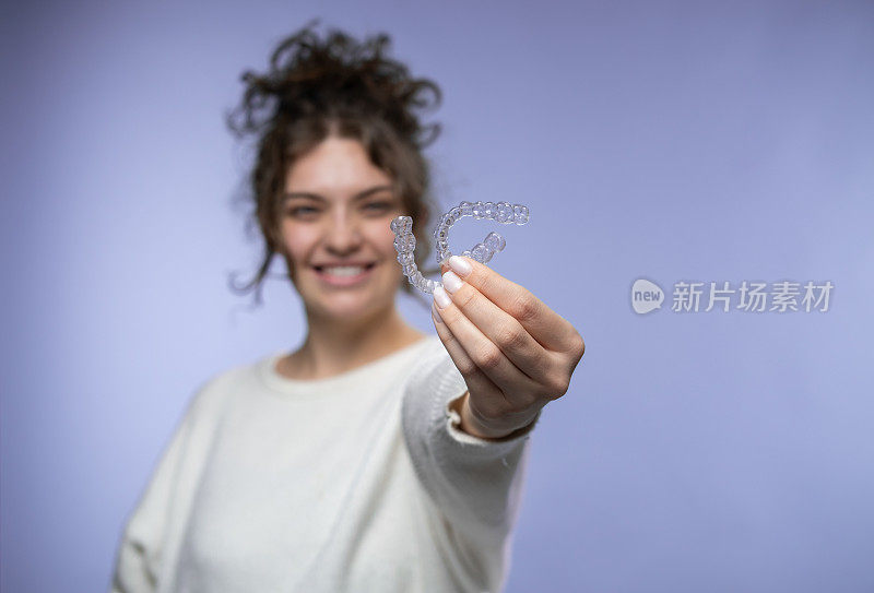 一位女士拿着隐形牙齿矫正器。