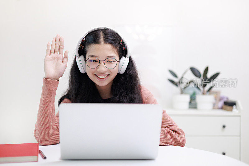 一个亚洲小女孩在家里用笔记本电脑和耳机在线学习。