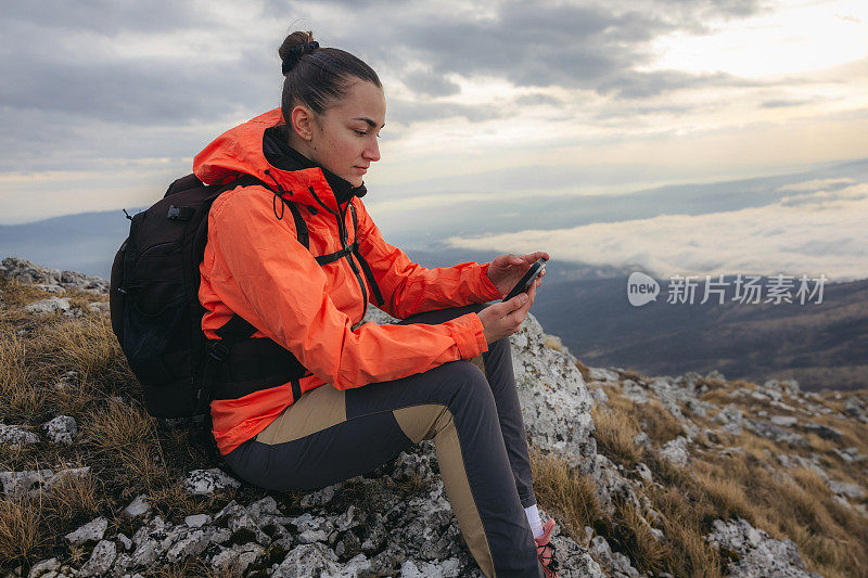 美丽的女徒步旅行者坐在山顶的岩石上