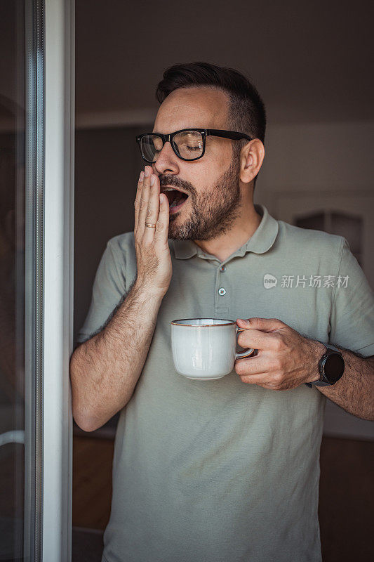 一位成年男子端着一杯咖啡，面带微笑地站在公寓的阳台门口