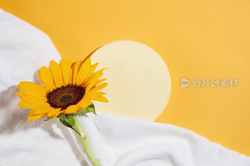 一个空的圆形底座，在黄色的背景下，一个角落用毛巾盖着，上面有一朵向日葵。照片是从俯视图拍摄的，有空间展示