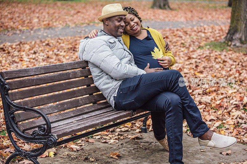 在公园里，一对幸福美丽的情侣坐在长椅上享受美好的秋日。