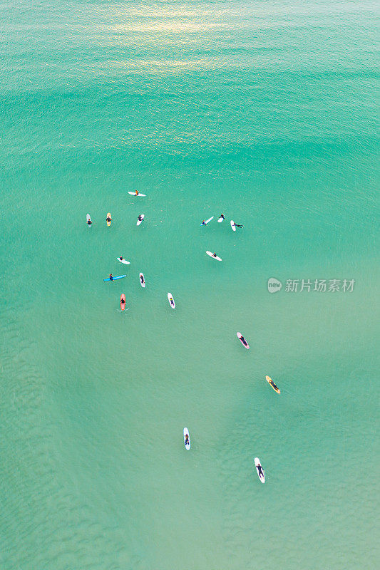 一群冲浪者在平静清澈的海面上等待一个浪头。