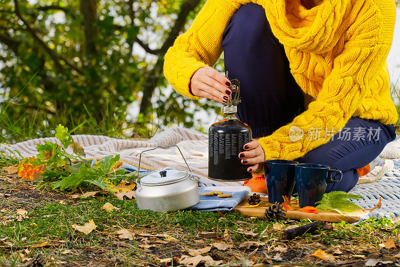 穿着黄色毛衣的年轻美丽的女孩在森林里用煤气炉煮咖啡。在秋天的森林里，用primus的火炉一步一步地煮咖啡