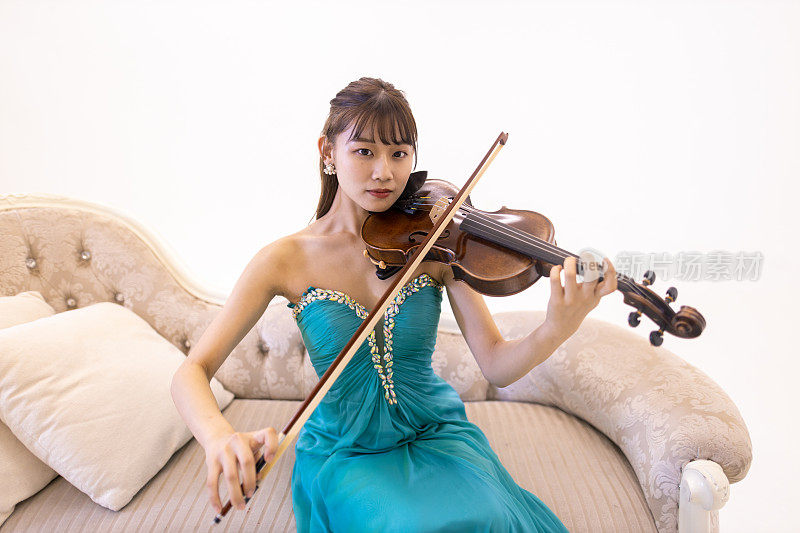 穿着绿松石蓝色衣服的年轻女子坐在沙发上拉小提琴