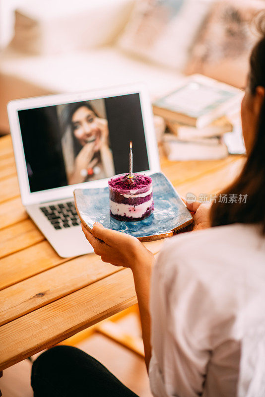 一位女士一边用笔记本电脑聊天，一边用生日蛋糕庆祝朋友的生日