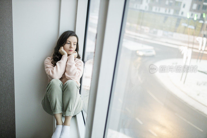 抑郁的女人在家里感到难过。女人悲伤地看着窗外。沮丧孤独的女人独自站在窗前看着窗外。