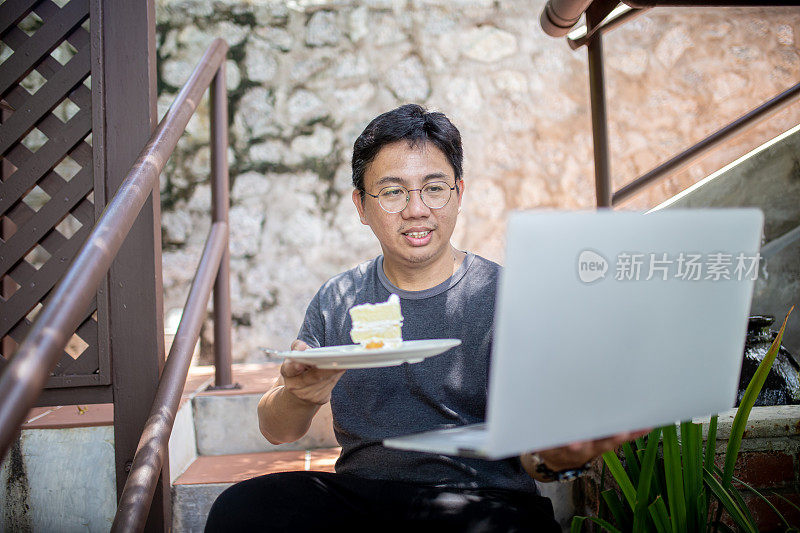 一名亚洲华人男子用视频会议的方式庆祝生日，并拿着一块生日蛋糕