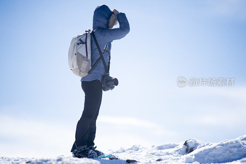 在山顶上，一个穿着雪鞋的女人望着地平线