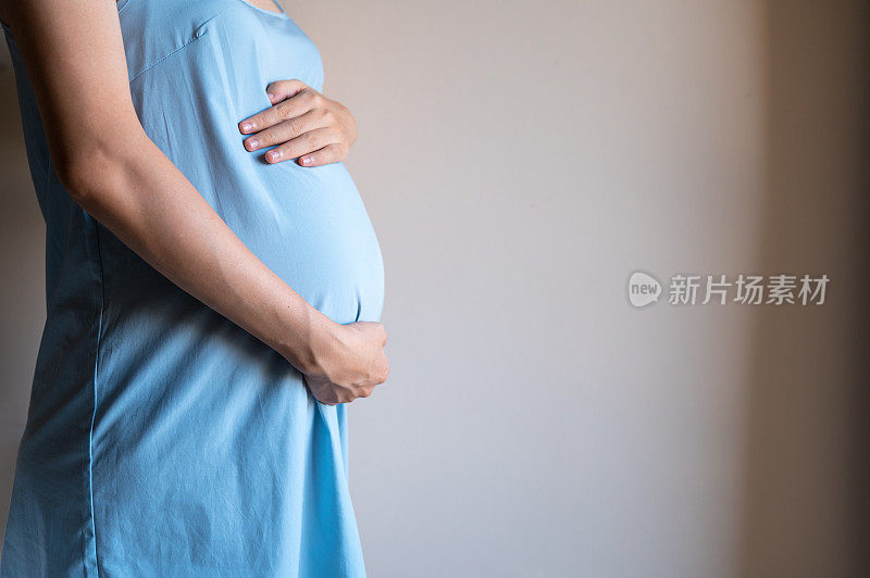一个孕妇抱着她的肚子在卧室靠墙