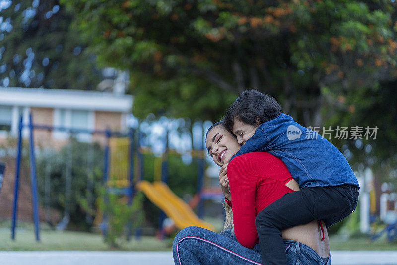 年轻的拉丁母亲和因疫情而独自一人的儿子在公园里拥抱，儿子亲吻母亲，一起玩耍