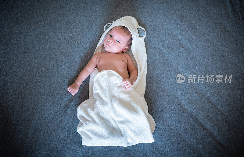 刚出生的男婴醒来，躺在床上，身上裹着一条毛巾，在卧室里
