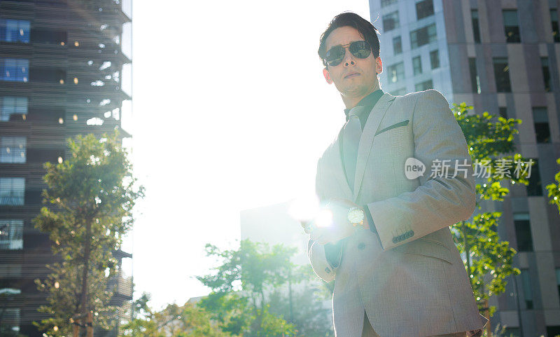 一个优雅的男人，穿着正式的西装，戴着墨镜，站在街道上，身后是阳光