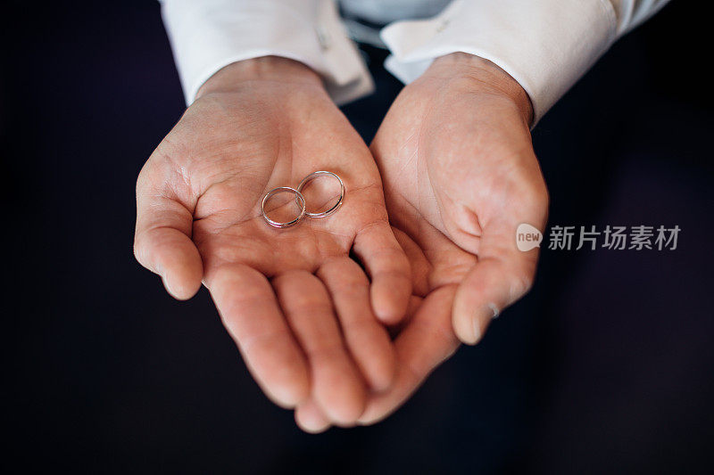 男人的手掌上握着结婚戒指，象征着结合和婚姻。创造幸福家庭和庆祝节日的理念。