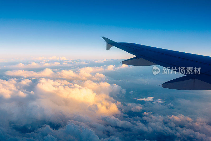 在飞行和旅行中，日落时分，从机翼上的舷窗往外看。飞机机翼下的大地和云层。飞行在天空。在飞行中俯瞰飞机机翼。