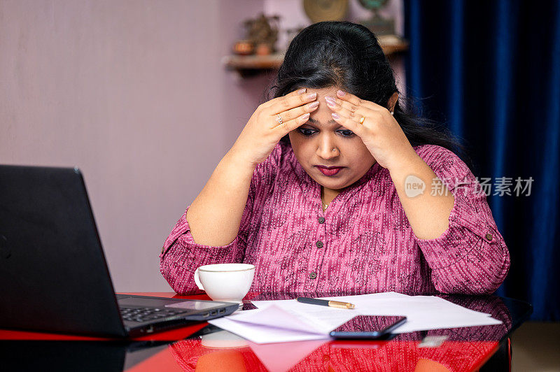 一个抑郁的女人在家里用笔记本电脑工作，她看起来很沮丧和不开心。