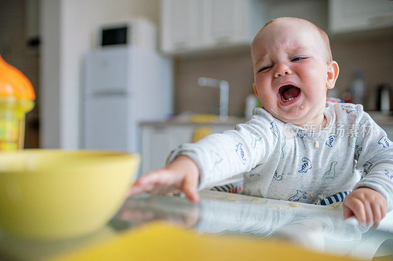 厨房桌子边一个哭闹的小男孩想去拿碗