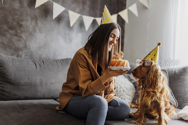 微笑的女人和她的狗在家里庆祝她的狗生日。