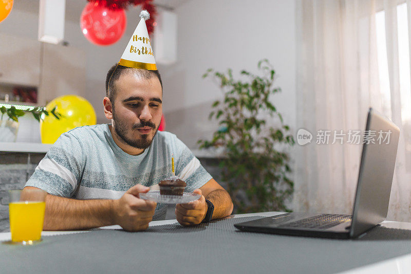 由于禁闭，一名年轻人在家里，在笔记本电脑前和朋友视频通话庆祝生日