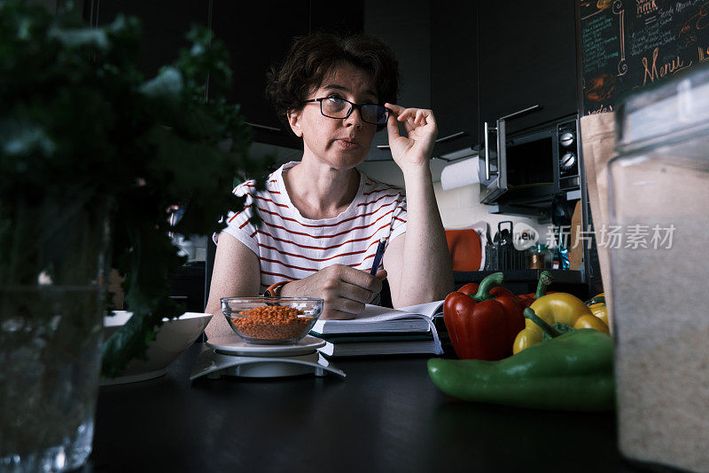 一名妇女正在家庭厨房里测量红扁豆并检查食谱