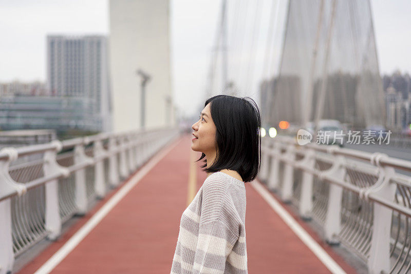 在市中心的一座桥上，一位亚洲妇女望着远方