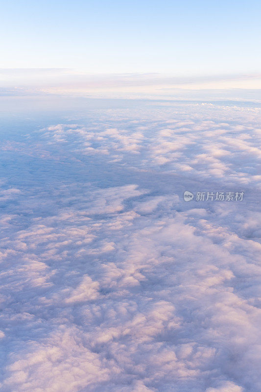 从飞机上俯瞰，淡黄色的日落在粉紫色浓密的云层上，头顶是蓝色的天空