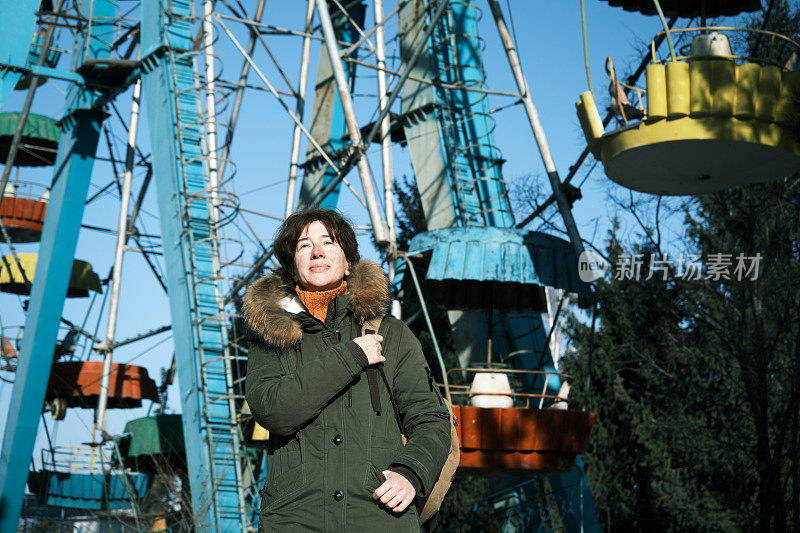 一名成年女子在冬季公园散步时，正看着一座古老的摩天轮