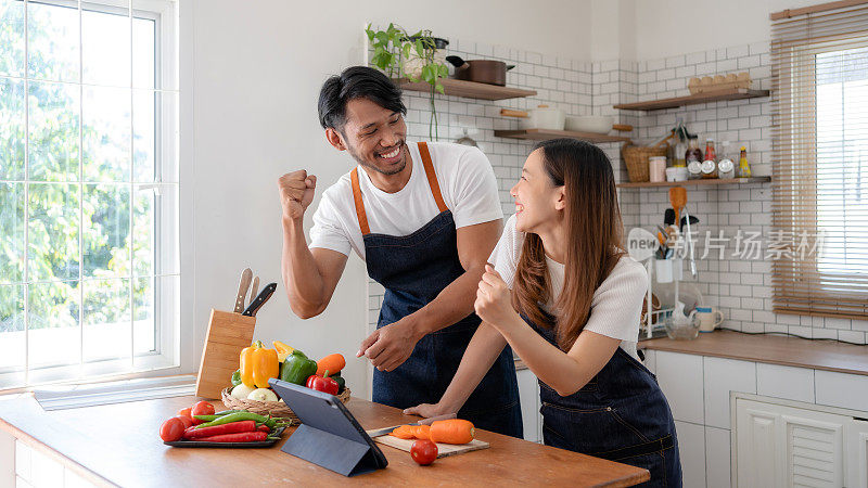 快乐的亚洲夫妇举起手臂庆祝成功完成在线烹饪课程