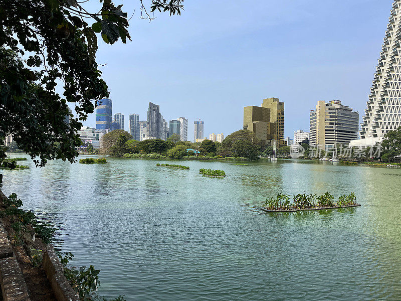 从斯里兰卡科伦坡贝拉湖对面的Gangaramaya公园俯瞰市中心的城市景观，牛郎星倾斜和垂直的塔，阳光明媚的蓝色晴空背景