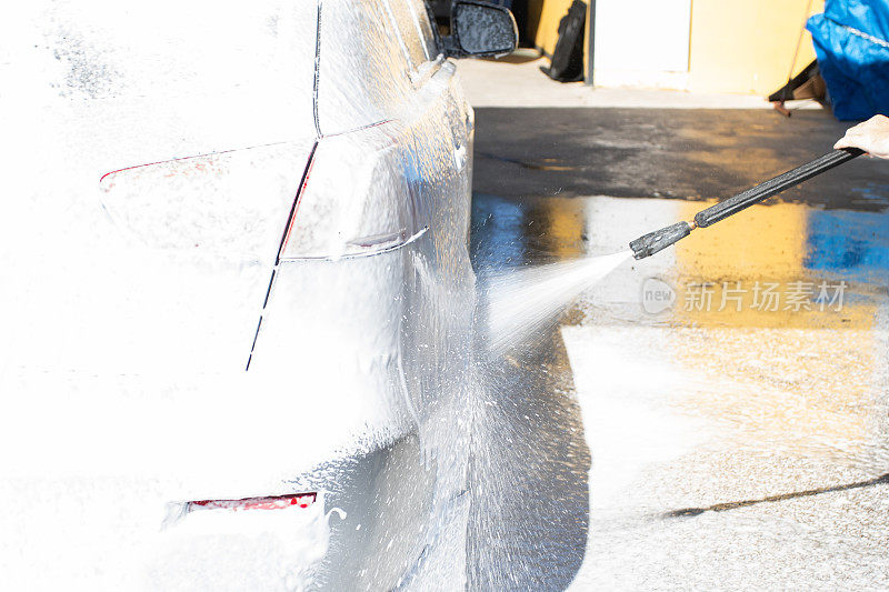 在压力下洗车，洗车工用洗车软管里的泡沫冲洗汽车
