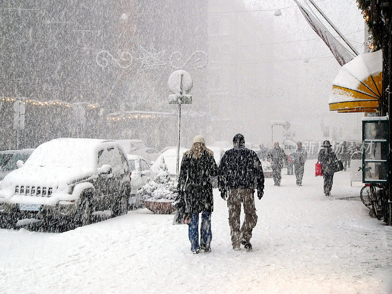 人们在暴风雪中走在城市的人行道上