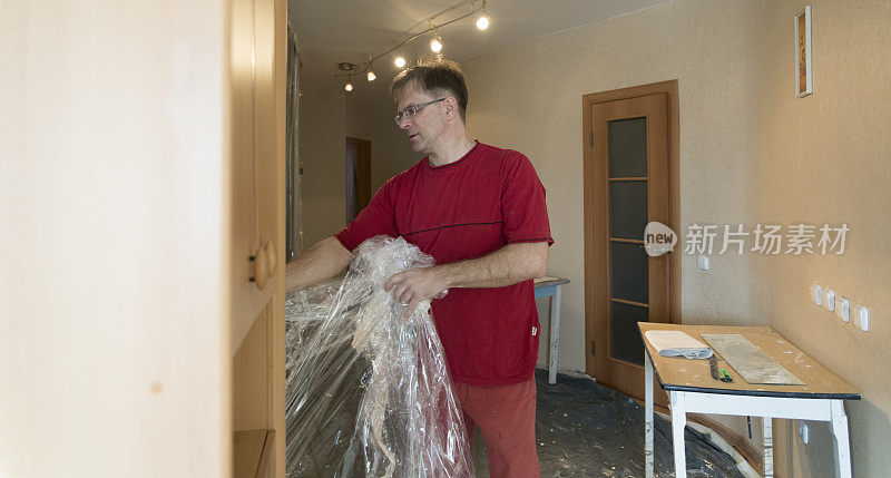 成熟男人覆盖家具的塑料保护膜为家居装修工程