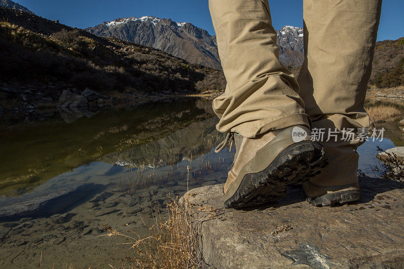观远足者的靴子站在湖边的岩石上