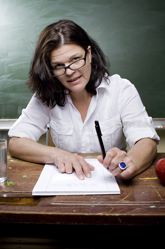 女教师坐在一张旧课桌前，正在写字
