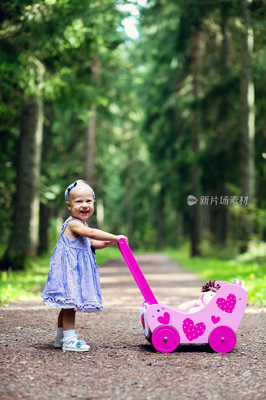 漂亮的小女孩推着她的娃娃婴儿车