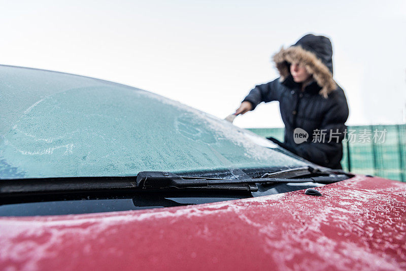 一个女人正在刮汽车挡风玻璃上的冰