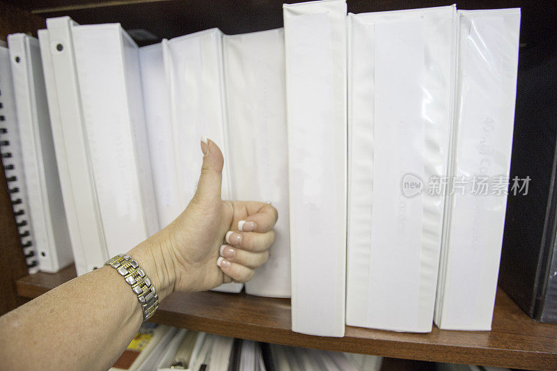 对着一架子的白色办公文件活页夹竖起大拇指