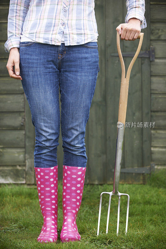穿着粉色惠灵顿鞋，手持花园叉子的女人