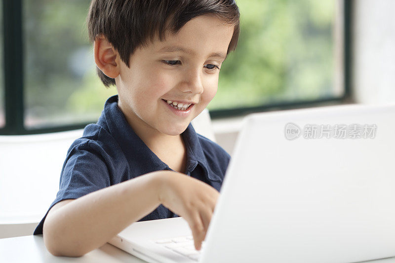 一个学龄前的男孩在用白色的笔记本电脑