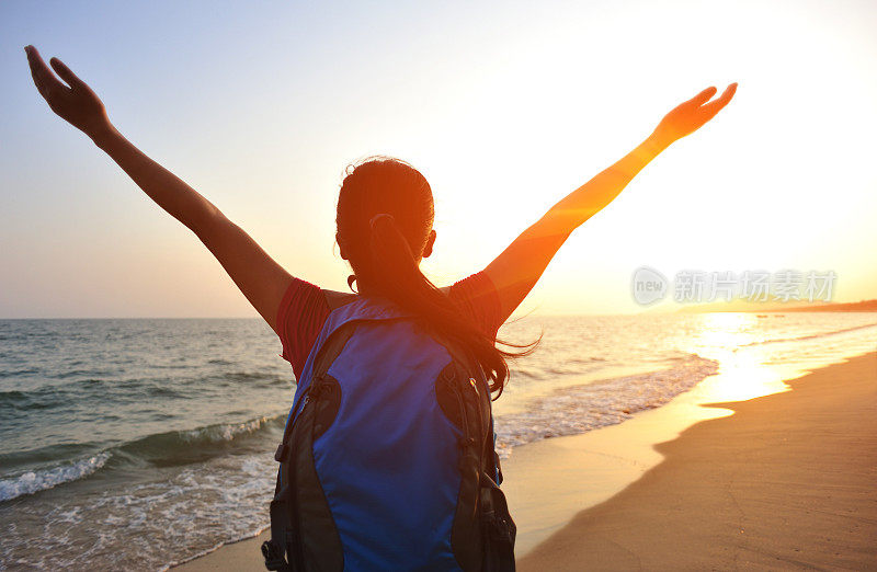 欢呼的女徒步旅行者在海边向夕阳张开双臂