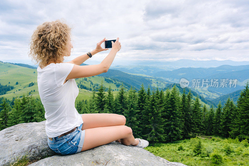 一名徒步旅行者在山顶用手机拍照