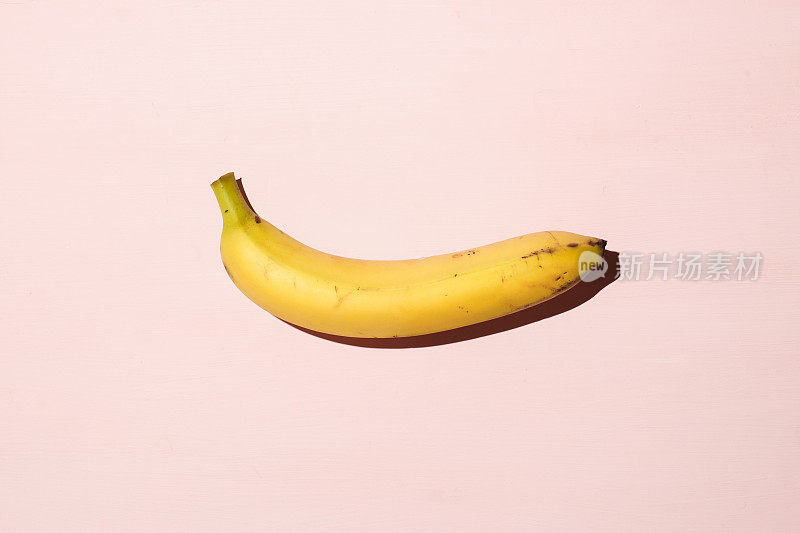 粉红色的桌子上放着甜多汁的香蕉。性生活，性欲和能力的概念。强光