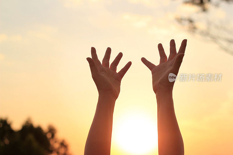 在夕阳的背景下，女人双手祈祷来自上帝的祝福