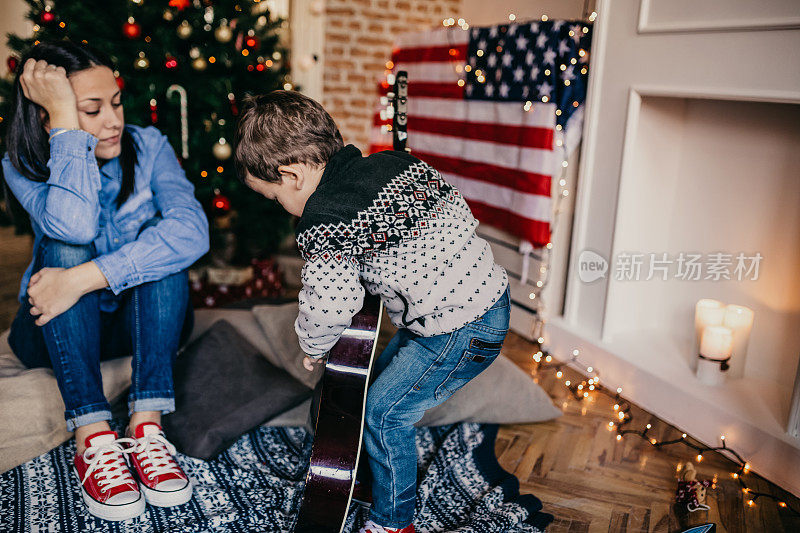 妈妈看着她的儿子在圣诞树前弹吉他