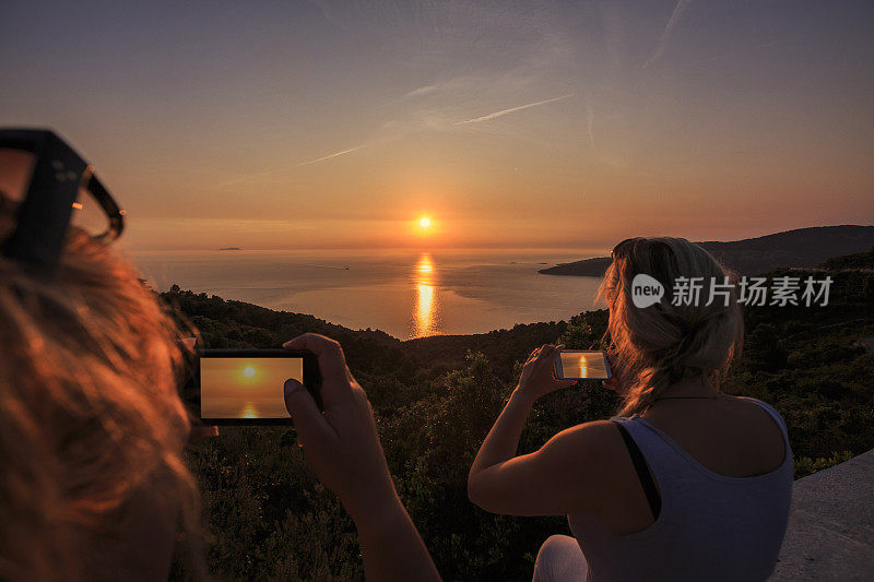 在日落的地中海，两名妇女用智能手机拍摄的渔船