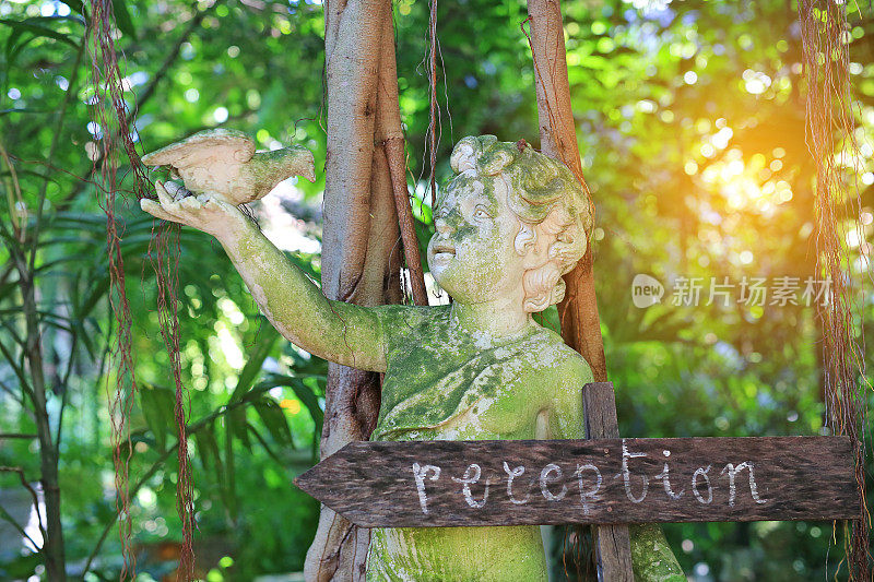 老婴儿雕像与鸟在花园里，接待标签的装饰，在绿色的树叶墙背景下，欧洲风格。