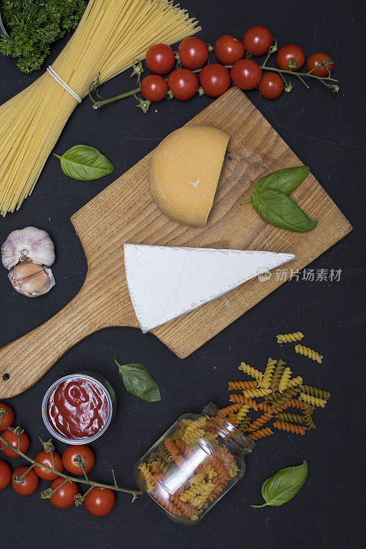 食物框架。面食配料。樱桃西红柿，意大利面，大蒜，罗勒，奶酪和香料在黑暗的背景，拷贝空间，俯视图