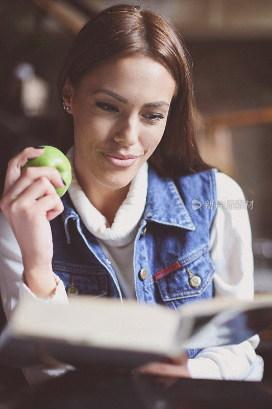 年轻的学生女孩在家里看书和吃苹果。
